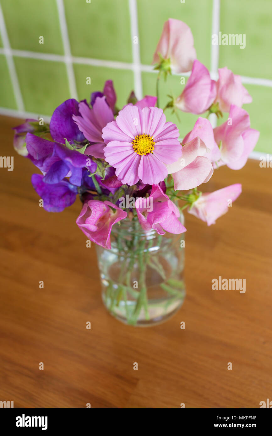 Gemischt, frischen Haufen Garten Blumen in einem Glas auf einem Küchentisch. Enge Tiefenschärfe mit Fokus auf Cosmos Blume. Stockfoto