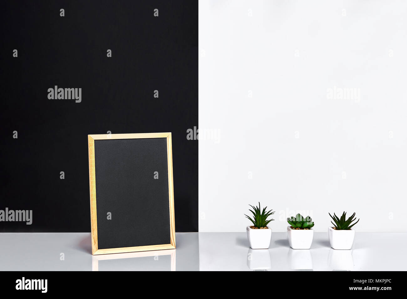 Holzrahmen mit schwarzen Platz für Text. Mock up. Stilvolle Inneneinrichtung. Grüne Pflanze in einem weißen Topf auf Schwarz-weiße Wand im Hintergrund Stockfoto