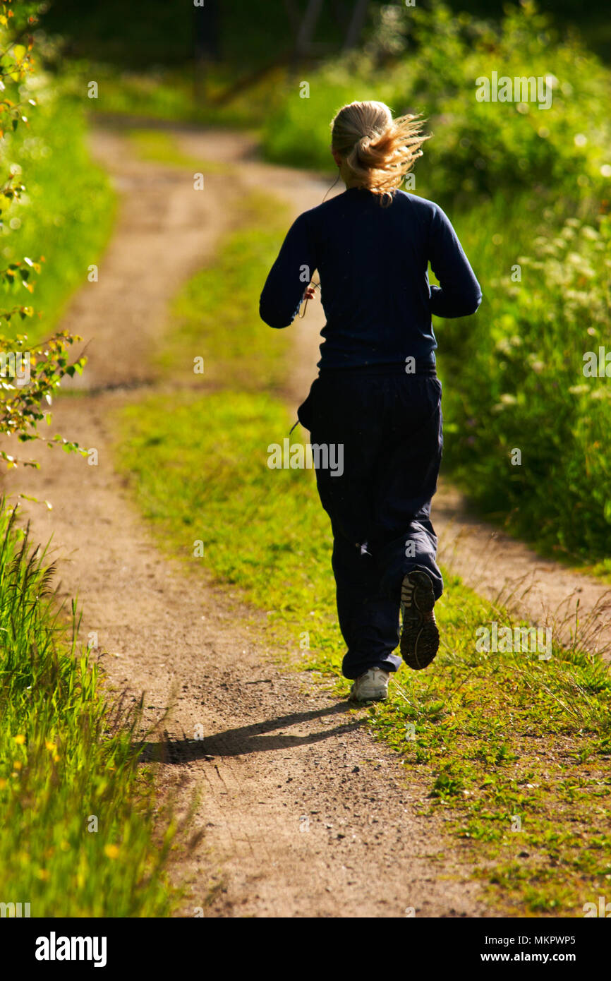Eine junge Frau Joggen in der Hintergrundbeleuchtung auf dem Track, umgeben von Grün. Übung verbessert die Gesundheit. Stockfoto