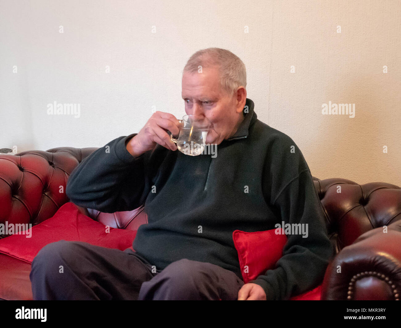 Reifer mann Trinkwasser leben allein auf einem Sofa sitzen Stockfoto