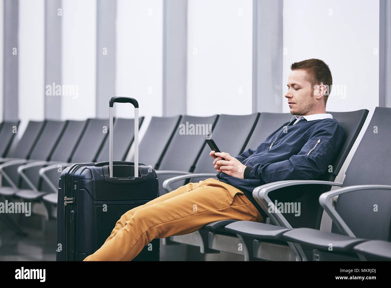 Mann mit dem Flugzeug reisen. Junge Passagier mit Telefon im Flughafen Terminal warten. Stockfoto