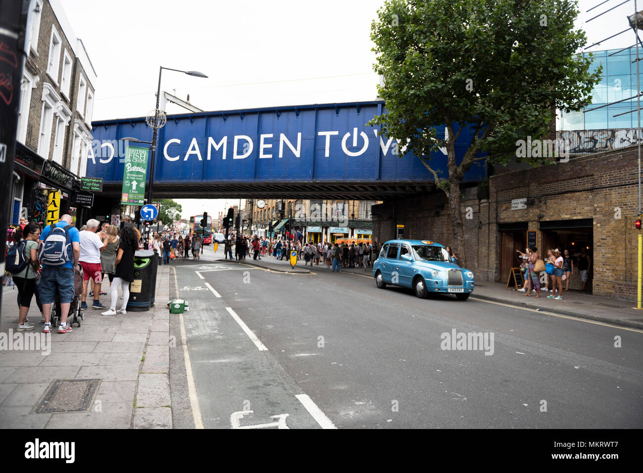 Blaue Taxi fährt durch Chalk Farm Road vorbei an der Camden Town Eisenbahnbrücke in Camden Town, London, UK. Stockfoto