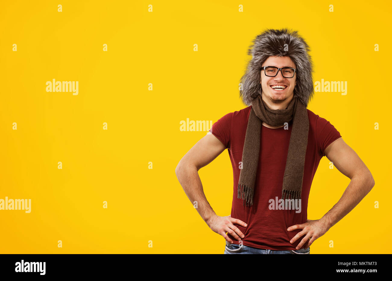 Lachend stilvollen Mann in T-Shirt und Winter Schal mit pelzigen Hut lächelnd an Kamera stehend auf gelben Hintergrund. Stockfoto