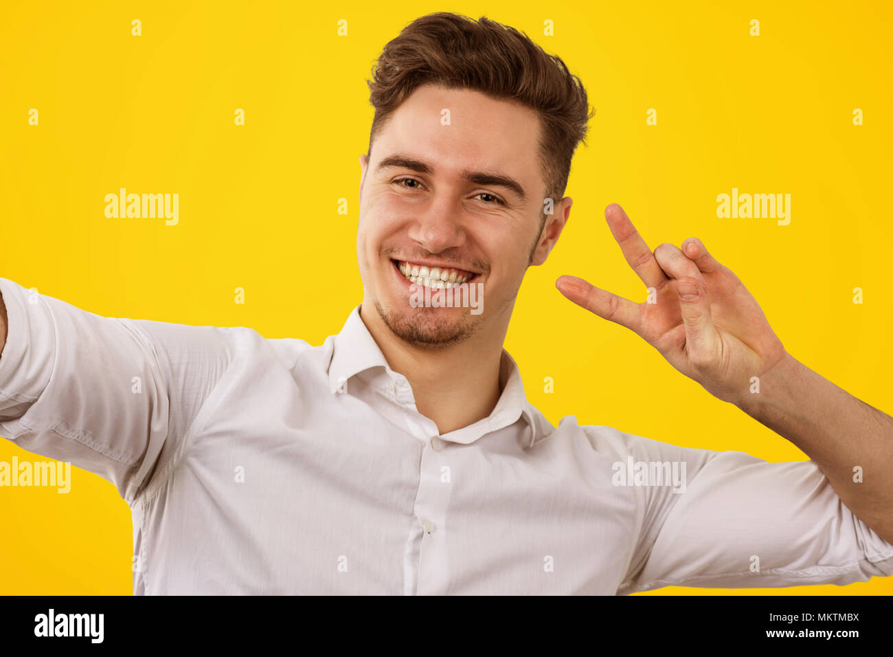 Stattliche glücklich Mann im weißen Hemd mit zwei Fingern und lächelnd an der Kamera auf gelben Hintergrund. Stockfoto