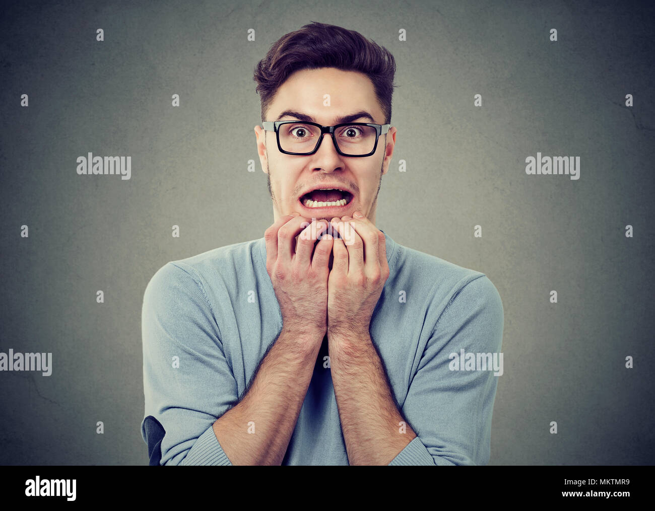 Junger Mann in Gläser, die panikattacke und Suchen mit Angst an der Kamera auf grauem Hintergrund. Stockfoto