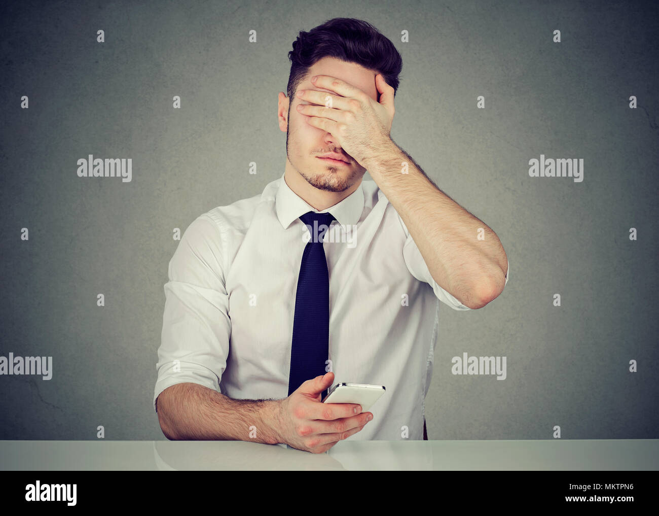 Junge formale Mann mit Telefon und für Gesicht, weil der Fehler während der Arbeit Stockfoto