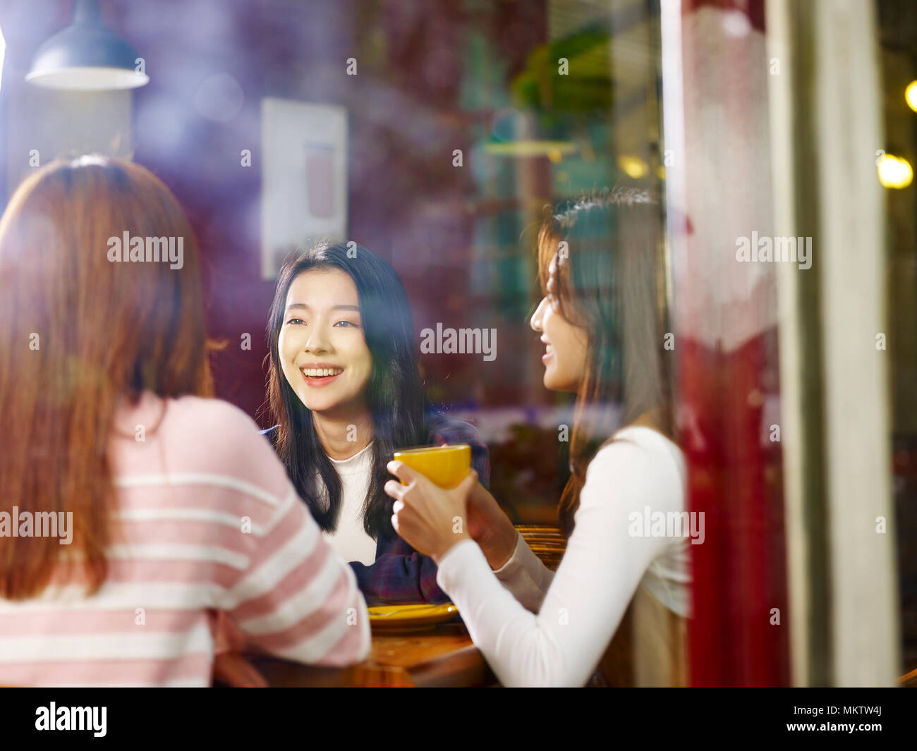 Drei glückliche wunderschöne junge asiatische Frauen am Tisch sitzen, plaudern, im Café oder Tee Haus, Schuß durch Fensterglas. Stockfoto