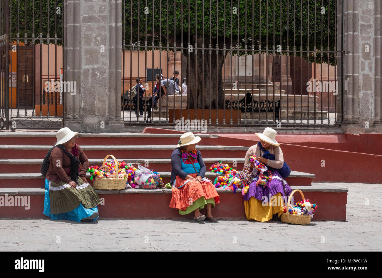Drei Sierra Otomi indische Frauen in streuen Hüte verkauft die farbenfrohen handgefertigten Kinder Puppen in San Miguel de Allende in Mexiko, Stockfoto