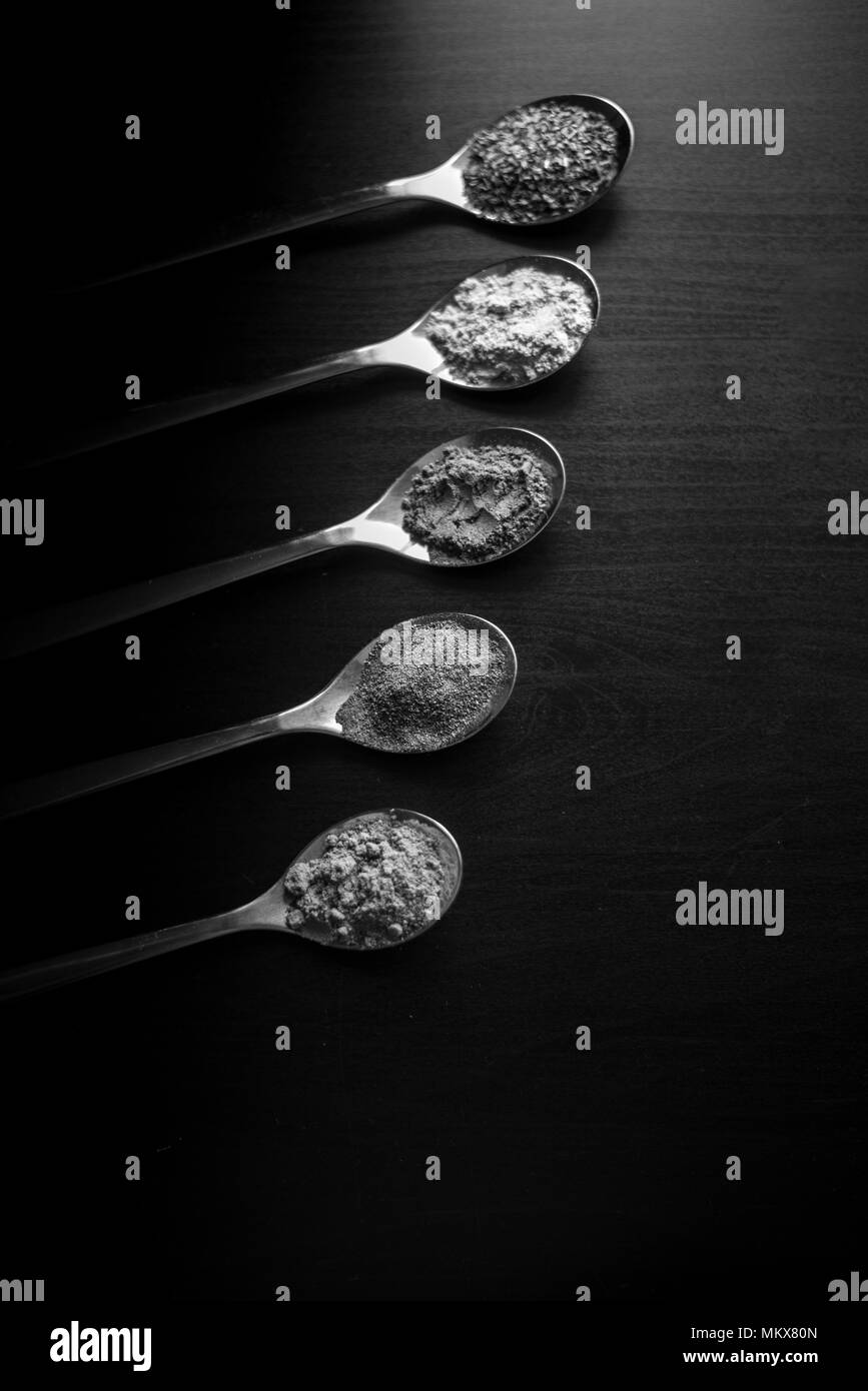 Gewürze farbige in Silber Löffel, auf einem schwarzen Holztisch gelegt. Pfeffer, Pfeffer, Salz, Basilikum, Senf Stockfoto