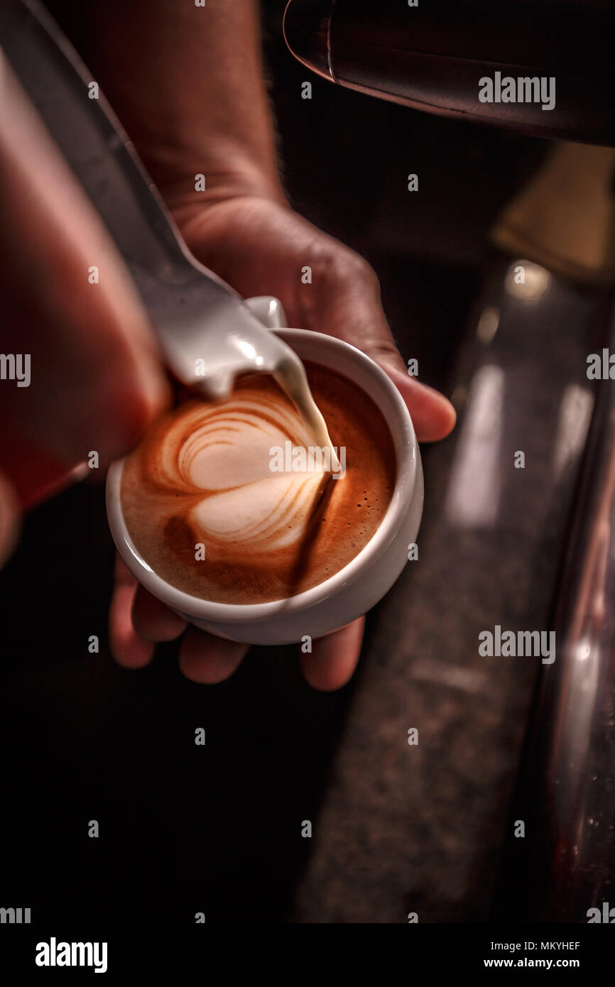 Barista gießen Milch für die Tasse Kaffee, latte Art vorbereiten, Kaffee Zubereitung und Service Konzept Stockfoto