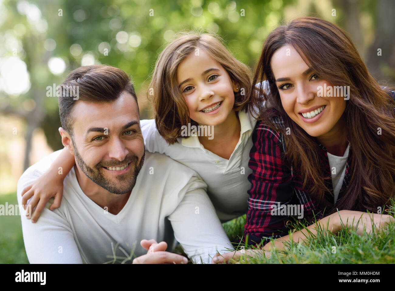 Glückliche junge Familie in einem städtischen Park. Vater, Mutter und Tochter Festlegung auf Gras. Stockfoto