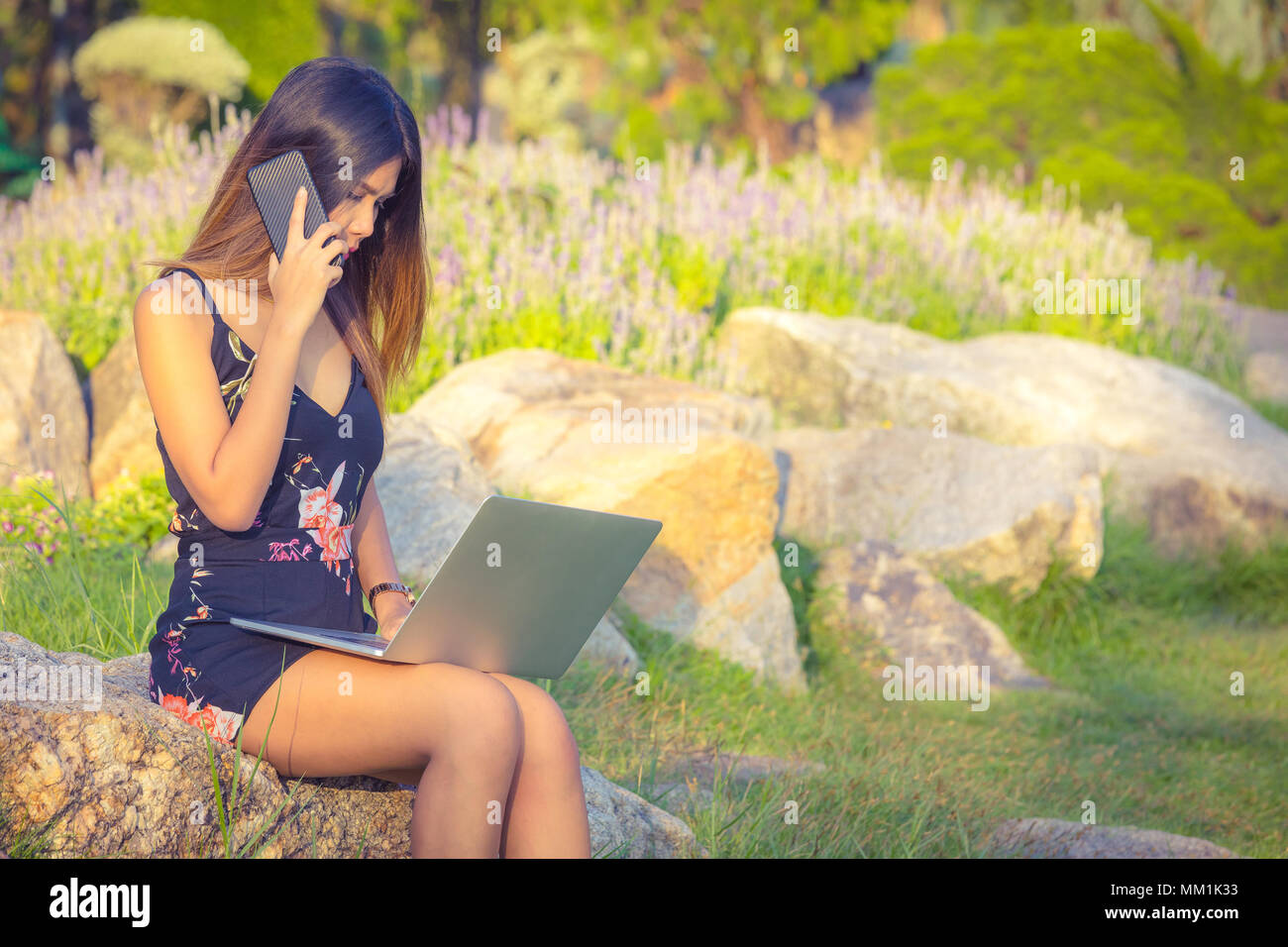 Attraktive Frauen mit Telefon und Laptop ein Stein in Park während des Tages sitzen Stockfoto