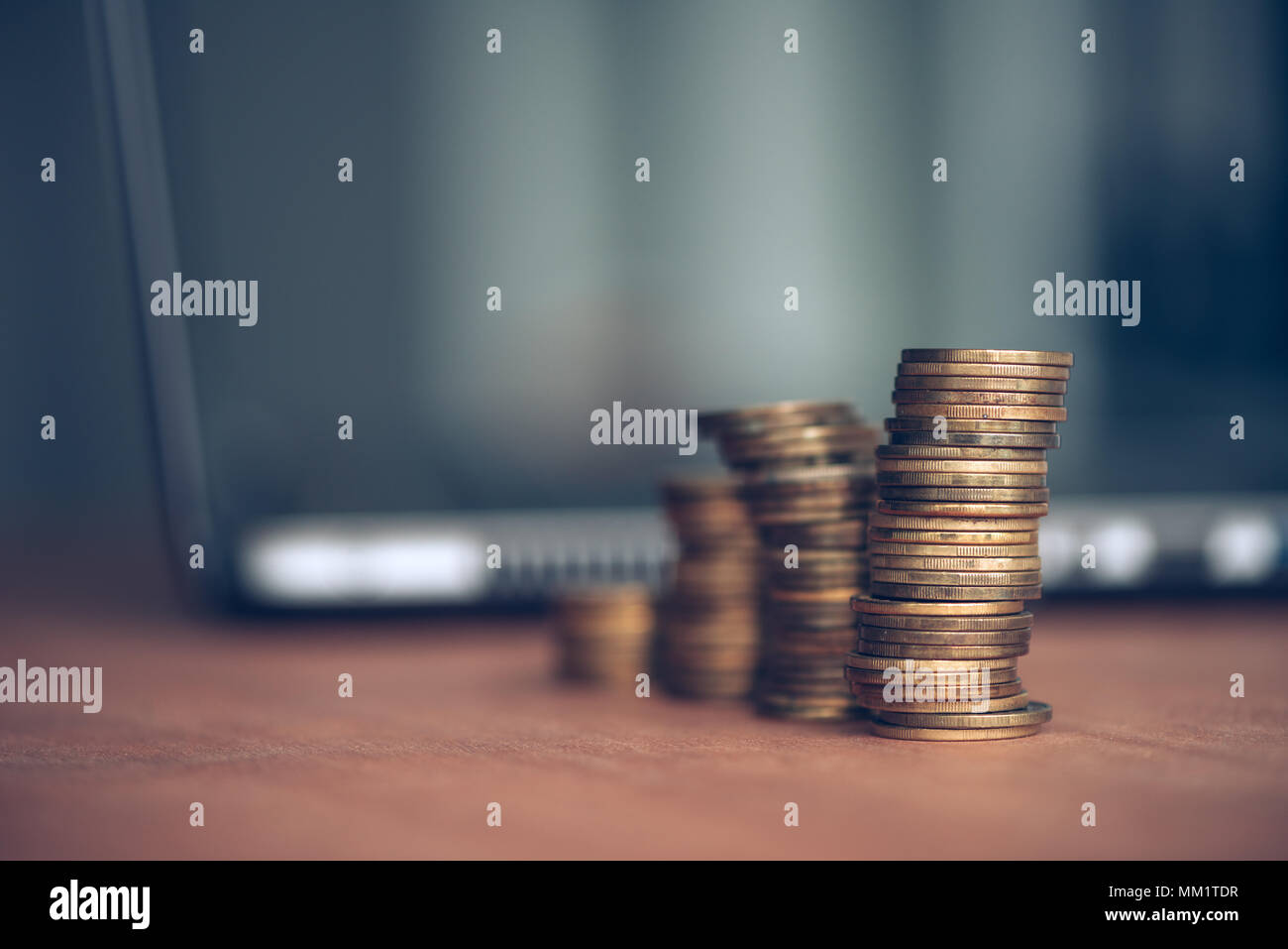 Gestapelte Säulen von Geld Münzen und Laptop Im defokussierten Hintergrund für Finanzen, Wirtschaft und Budgetierung Konzept Stockfoto