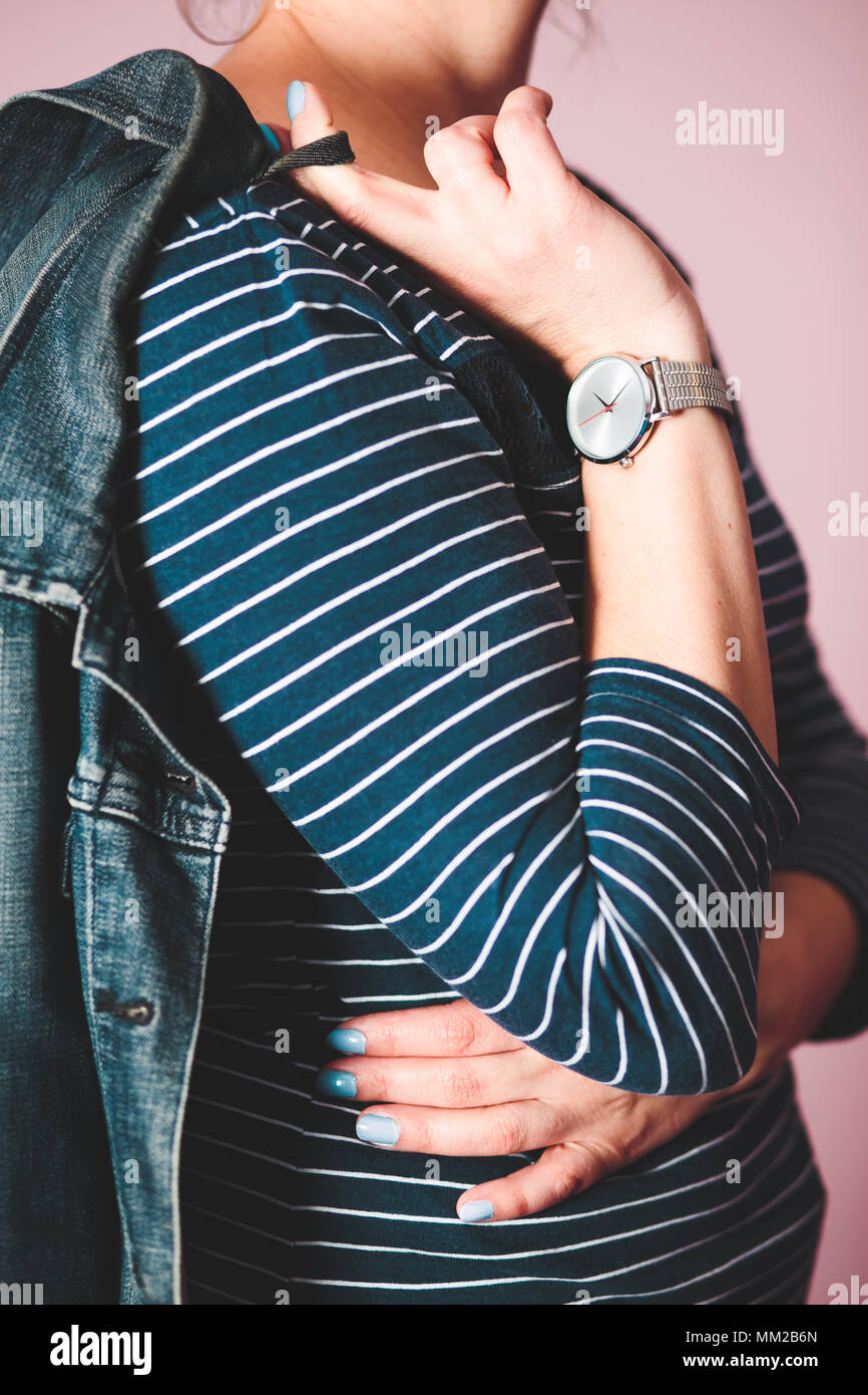 Frau silber Armbanduhr und blauen Bluse in Weiß-Streifen, Jeans Jacke. Stand vor der Pastell rosa Wand Stockfoto