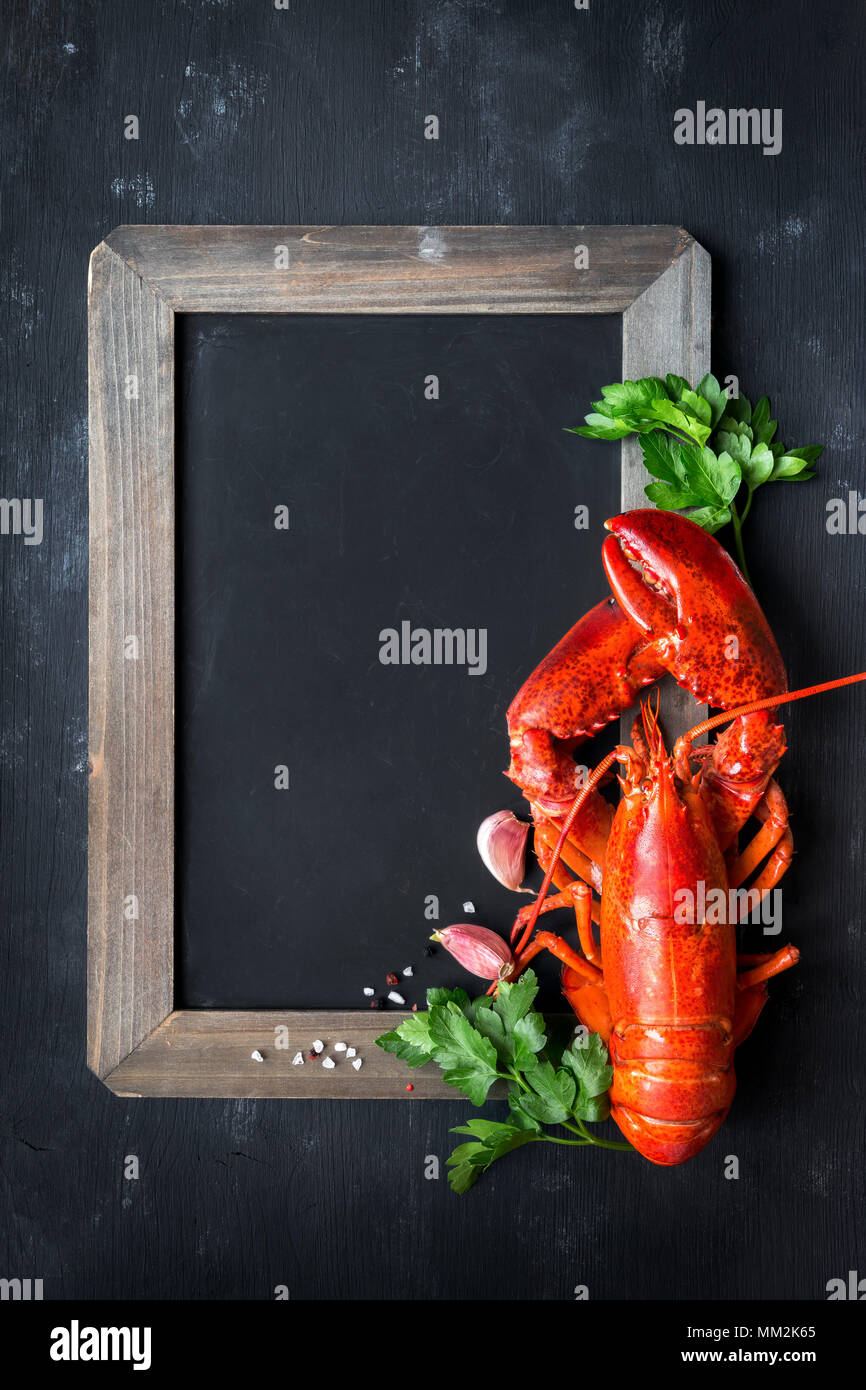 Ganze Red Lobster mit frischer Petersilie, Knoblauch, Salz und Pfeffer Bohnen auf Leere Schwarze Schiefertafel auf schwarzem Hintergrund. Ansicht von oben mit vielen c Stockfoto