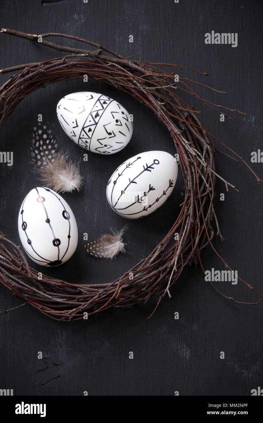 Ostern Konzept mit einem rustikalen handgefertigte Kranz und drei dekorierten Eier gegen blask Holz- Hintergrund Stockfoto