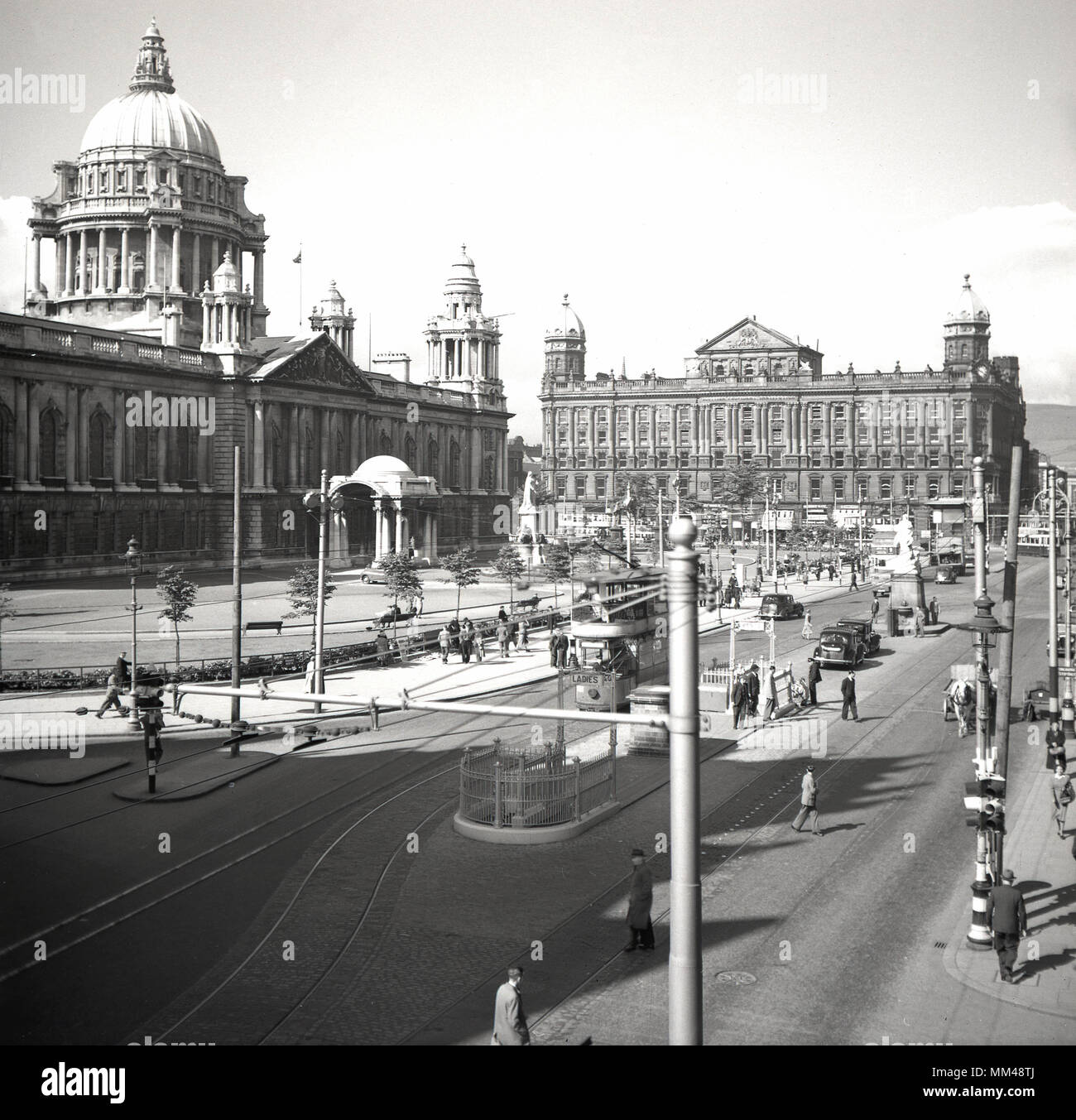 1950er Jahre, historisches Bild des Stadtzentrums von Belfast, Nordirland in dieser Zeit. Ein Blick über den Donegall Square, der die großartige Struktur des Belfast City Hall zeigt, ein beeindruckendes öffentliches oder bürgerschaftliches Gebäude, das 1906 im barocken Revival-Stil fertiggestellt wurde. So wie die allgemeine Aktivität, können wir sehen, dass die Straßenbahnen noch in Betrieb sind. Stockfoto