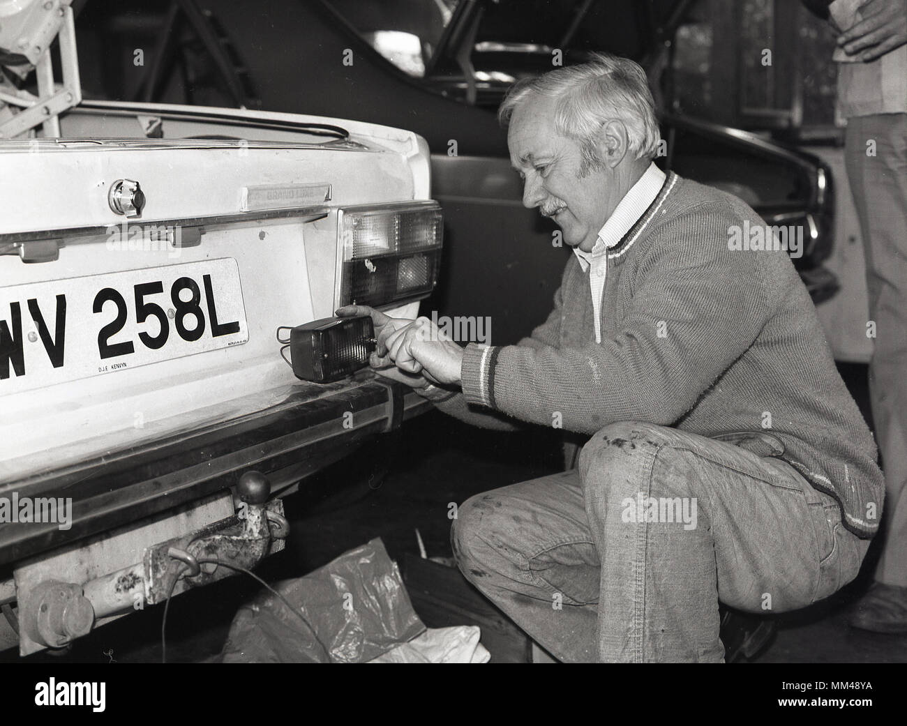 1970 s, historischen, ein Mann an einer Erwachsenenbildung klasse Auto Instandhaltung oder Wartung, Knieten während der Arbeit auf der Rückseite Lichter eines Volvo motorcar, England, UK. Stockfoto