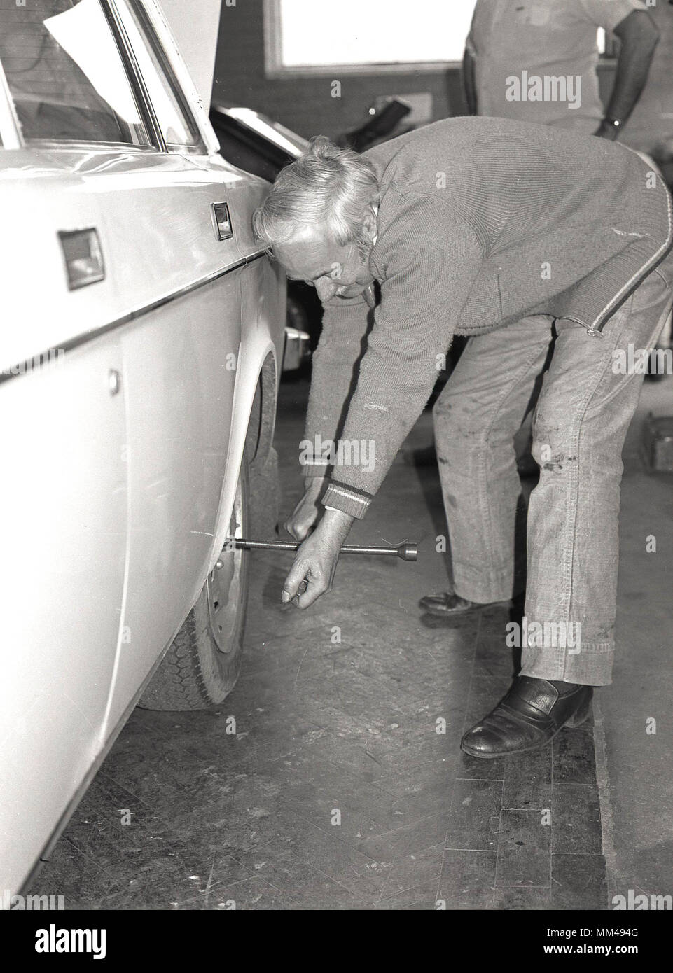 1970 s, historische Bild, reifen Mann mit normalen Kleidung mit Schraubenschlüssel in der Hand nach unten biegen der Radmuttern auf ein Kraftfahrzeug in einem Erwachsenenbildung Auto Wartung Kurs zu entfernen, England, UK. Weiterbildung Rentner' war besonders ermutigt, aktiv und neue Fähigkeiten zu erlernen. Stockfoto