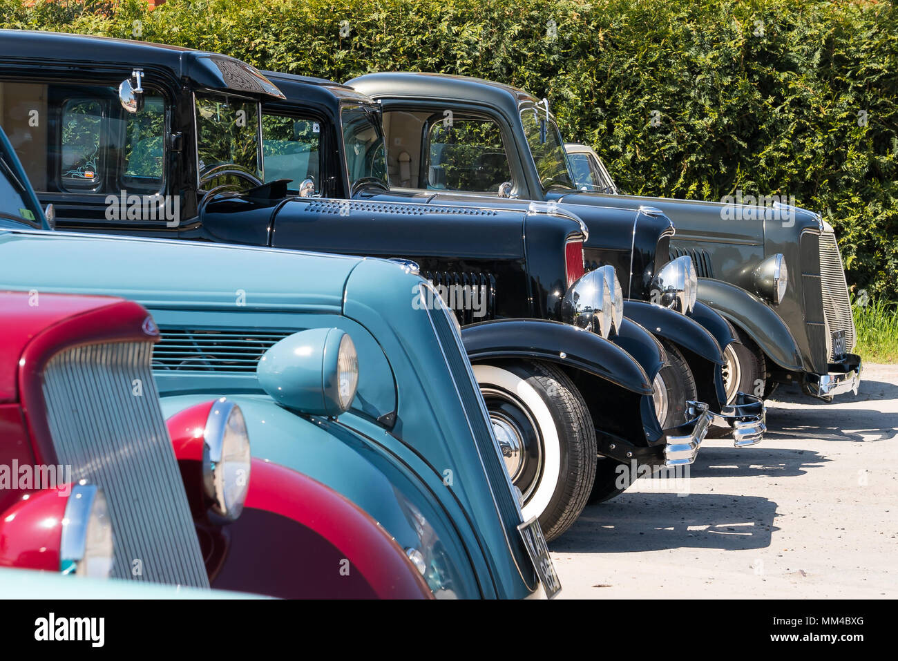 Glänzend poliert, Hot Rods geparkten Seite an Seite, draußen in der Sonne. Sammlung von alten, klassischen, amerikanischen Autos, von der Seite, die vorderen Stoßstangen genommen. Stockfoto