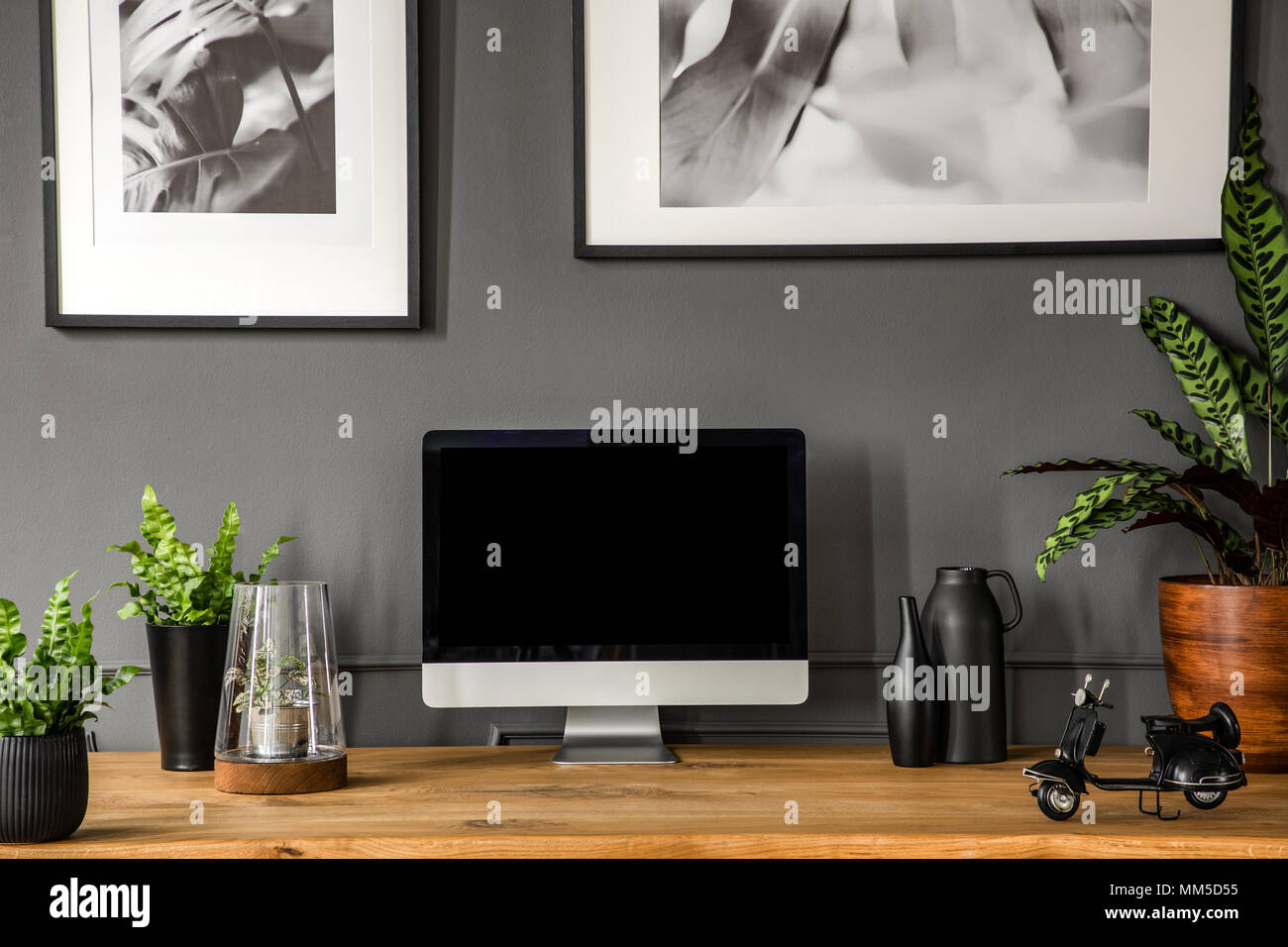 Pflanzen und schwarz computer monitor am Schreibtisch aus Holz in Grau home office Interieur mit Poster Stockfoto