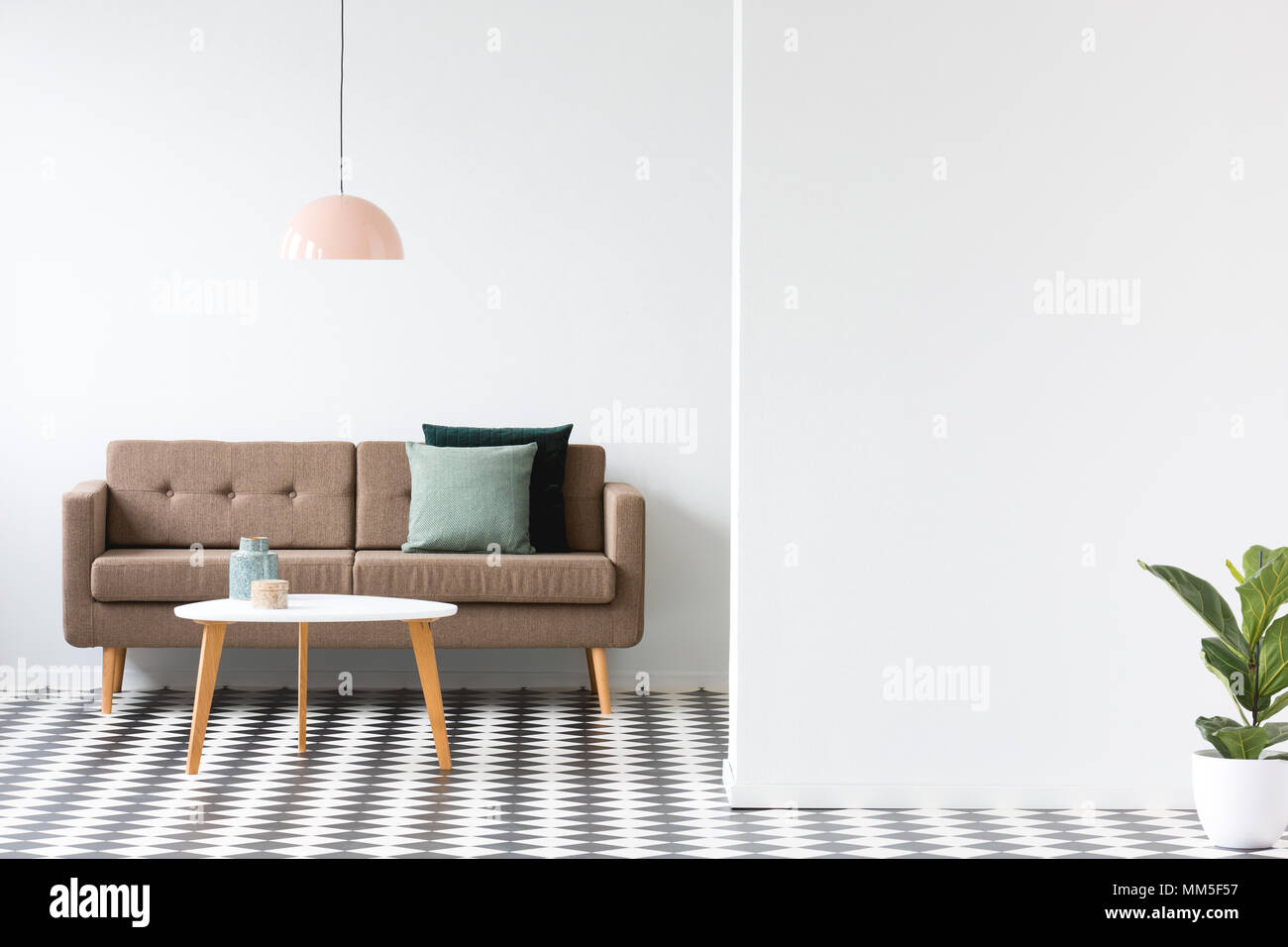 Runder Tisch vor einem braunen Sofa unter Pastell Lampe in minimalen Wohnzimmer Innenraum Stockfoto