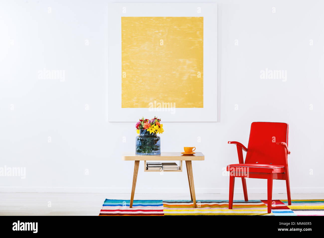 Roten Sessel neben einem hölzernen Tisch mit Blumen auf bunten Teppich im Wohnzimmer Einrichtung mit gelben Anstrich Stockfoto