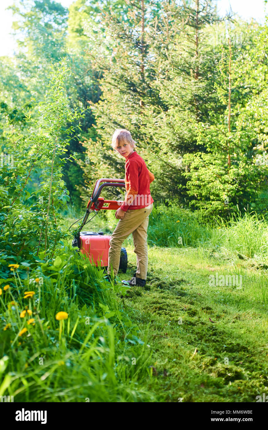 Kind Junge Helfen im Garten mähen Rasen mit einem Rasenmäher Stockfoto