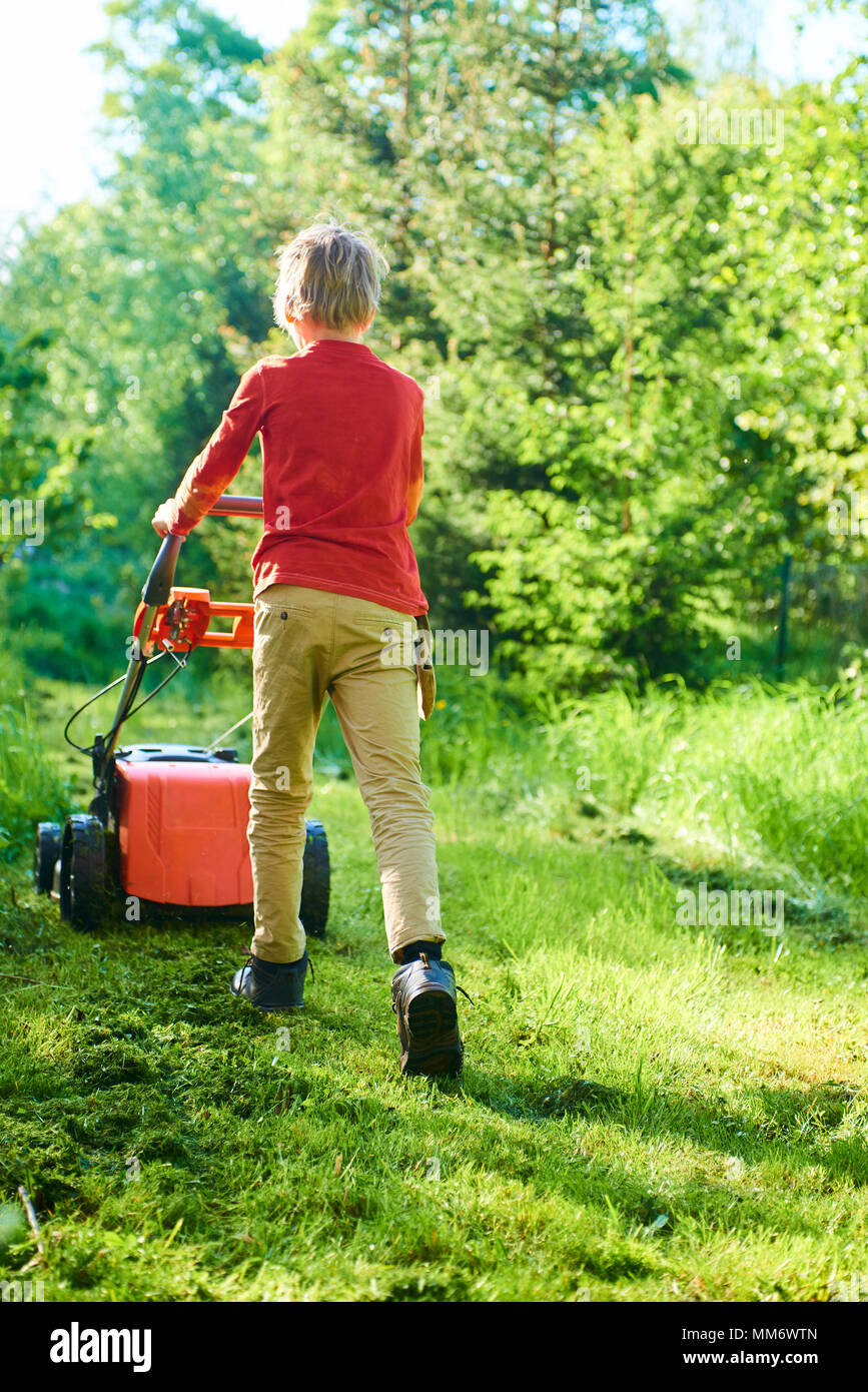 Kind Junge Helfen im Garten mähen Rasen mit einem Rasenmäher Stockfoto