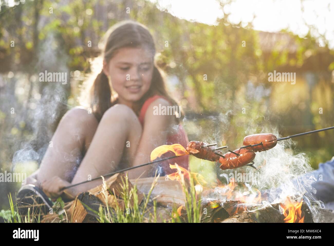 Kinder genießen, Lagerfeuer. Toasten Mädchen Würstchen auf den Garten. Stockfoto