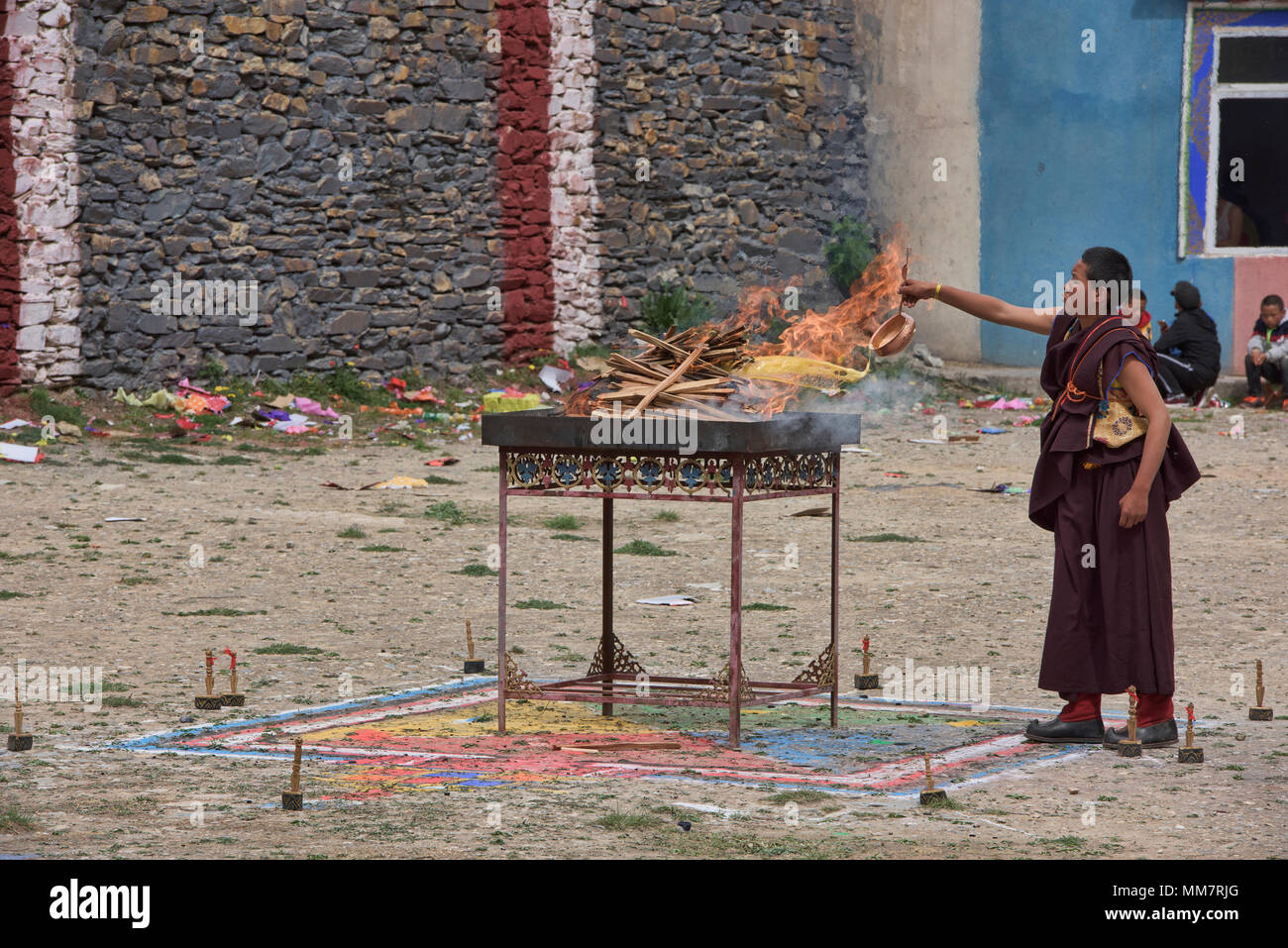 Tibetischen Mönch legt yak Butter auf dem Feuer am Jinganqumo Reinigung Festival in Dege, Sichuan, China Stockfoto