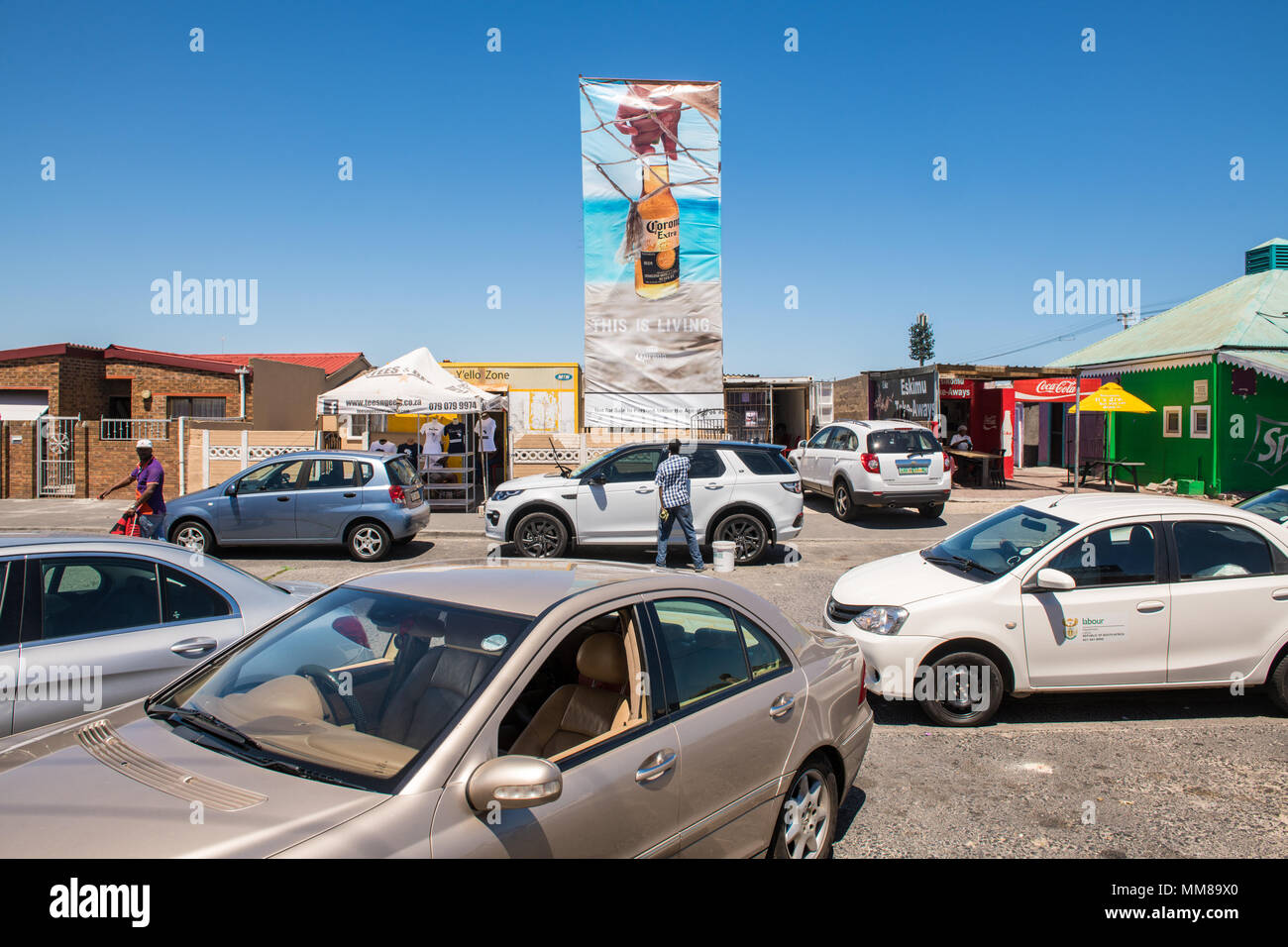 Ein Cluster von Autos sitzt außerhalb der lokalen Unternehmen wie Menschen Mühle in Guguletu Township in Kapstadt, Südafrika Stockfoto