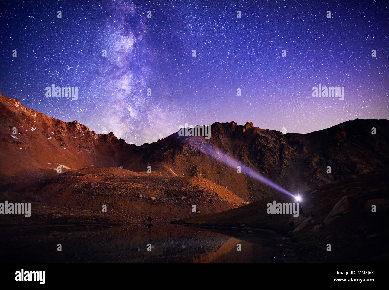 Mann mit Scheinwerfer in den Bergen am wunderschönen Nachthimmel mit Sternen und der Milchstraße Stockfoto