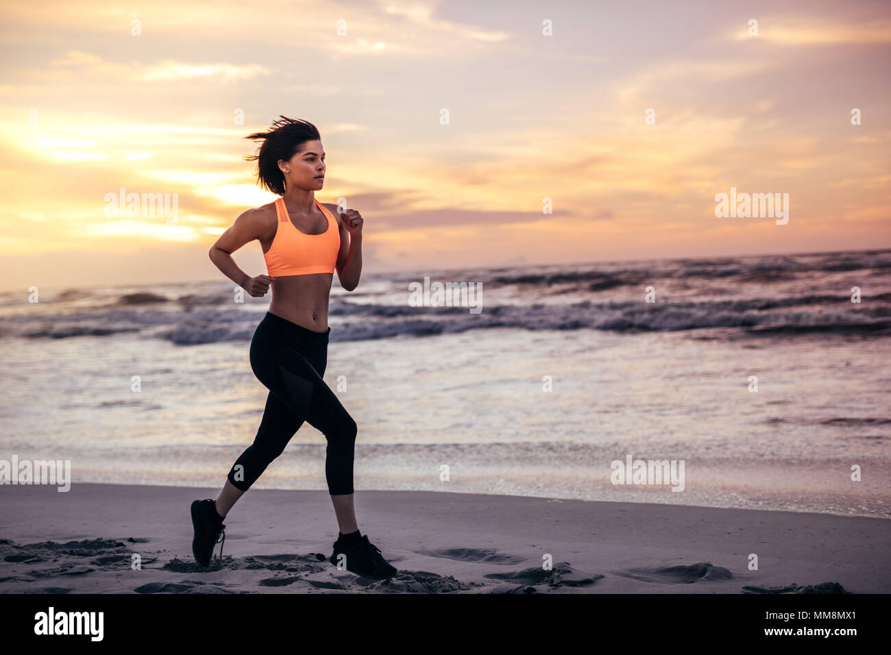 Sportlerin am Strand entlang am Morgen läuft. Frau im laufenden Outfit Sprinten am Ufer des Meeres. Stockfoto