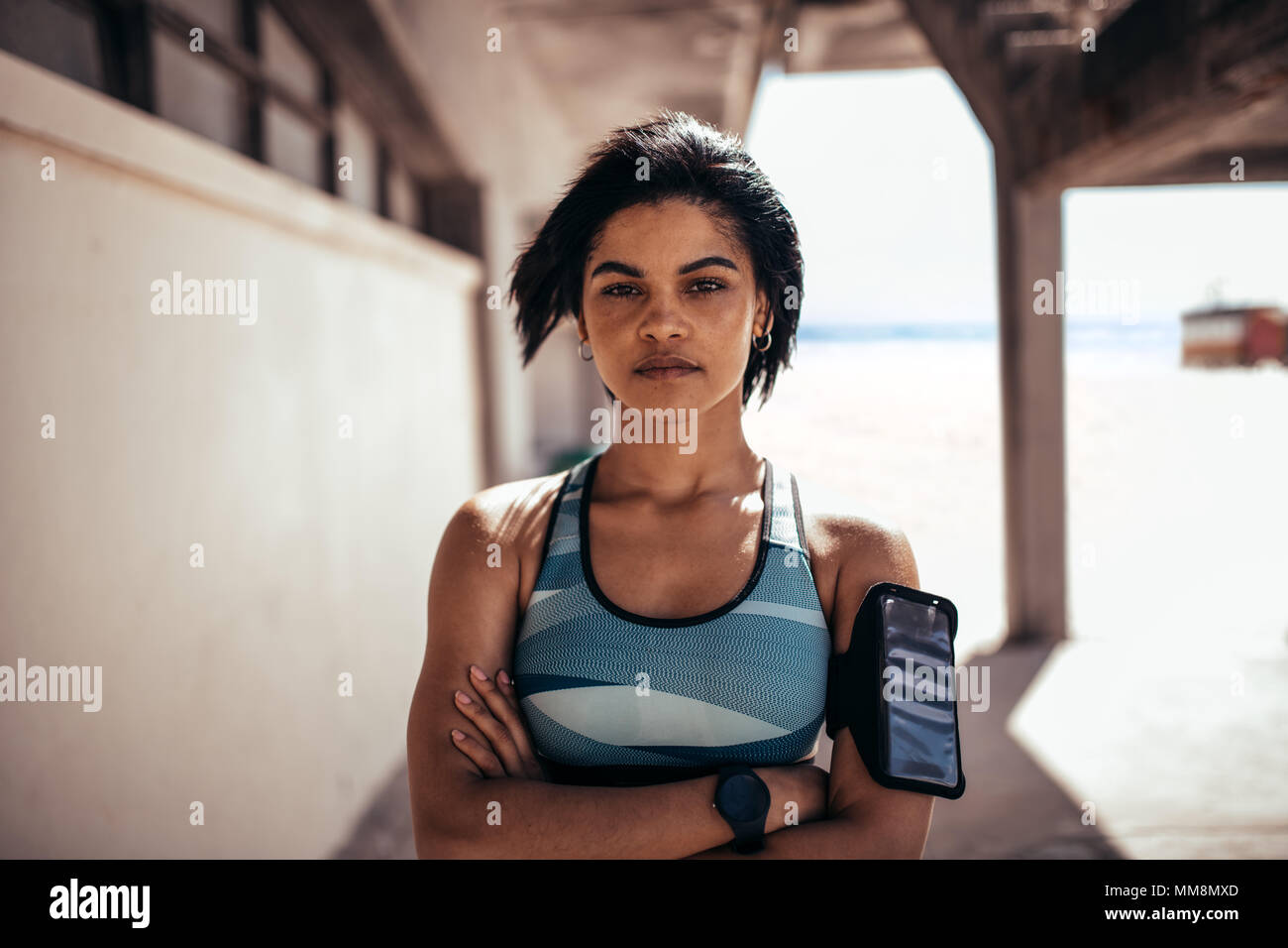 Portrait von selbstbewusste Frau Athleten stehen im Freien mit verschränkten Armen und Kamera. Mit Handy weiblichen am Armband eine Pause Stockfoto