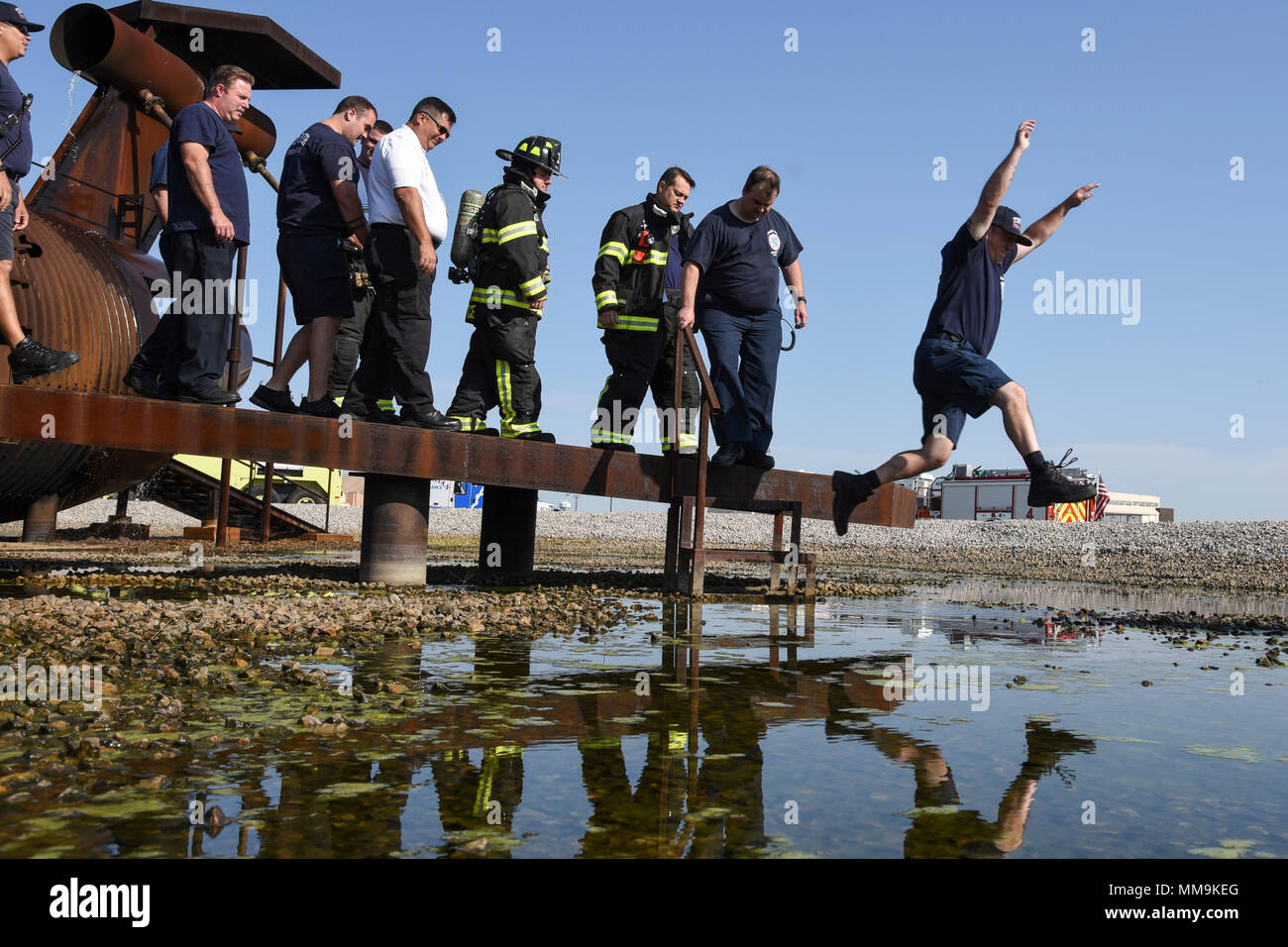 Jerol Williams Sprünge über einen Pool von Wasser neben dem Flugzeug Fire Training Gerät nach einer Sicherheitseinweisung, bevor er und die anderen Mitglieder der 72nd Bauingenieur Squadron, Feuerwehr, beginnen Ausbildung Sept. 13, 2017, Tinker Air Force Base, Oklahoma. Die Feuerwehrmänner wurden auch von den Mitgliedern des Internationalen Flughafen Tulsa Feuerwehr, die Rezertifizierung für ihre Mitglieder durchgeführt. (U.S. Air Force Foto/Greg L. Davis) Stockfoto