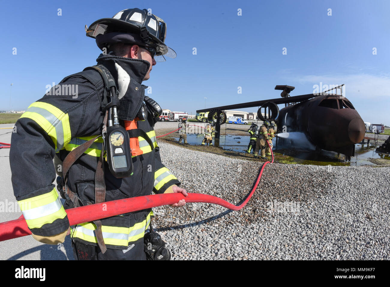 Ein 72Nd Bauingenieur Squadron Feuerwehrmann dazu neigt, eine rote Hand - Schlauch während einer Schulungsveranstaltung im Full-size Flugzeugbrand Trainingsgerät auf dem Flugplatz entfernt Sept. 13, 2017, Tinker Air Force Base, Oklahoma. Feuerwehrmänner von Tinker AFB wurden von den Mitgliedern der Internationalen Flughafen Tulsa Feuerwehr während der jährlichen Rezertifizierung verbunden. (U.S. Air Force Foto/Greg L. Davis) Stockfoto
