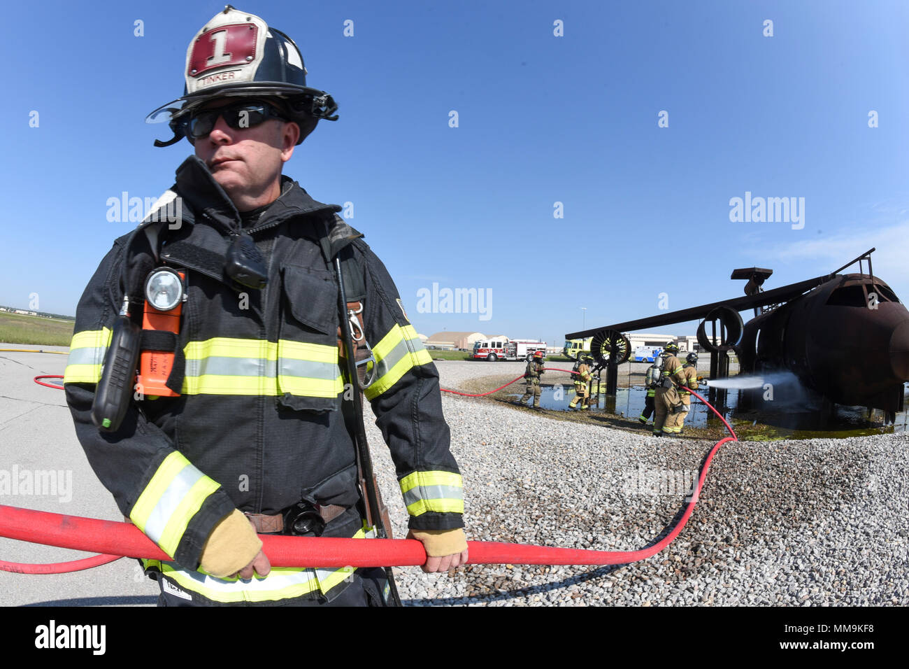 Ein 72Nd Bauingenieur Squadron Feuerwehrmann dazu neigt, eine rote Hand - Schlauch während einer Schulungsveranstaltung im Full-size Flugzeugbrand Trainingsgerät auf dem Flugplatz entfernt Sept. 13, 2017, Tinker Air Force Base, Oklahoma. Feuerwehrmänner von Tinker AFB wurden von den Mitgliedern der Internationalen Flughafen Tulsa Feuerwehr während der jährlichen Rezertifizierung verbunden. (U.S. Air Force Foto/Greg L. Davis) Stockfoto
