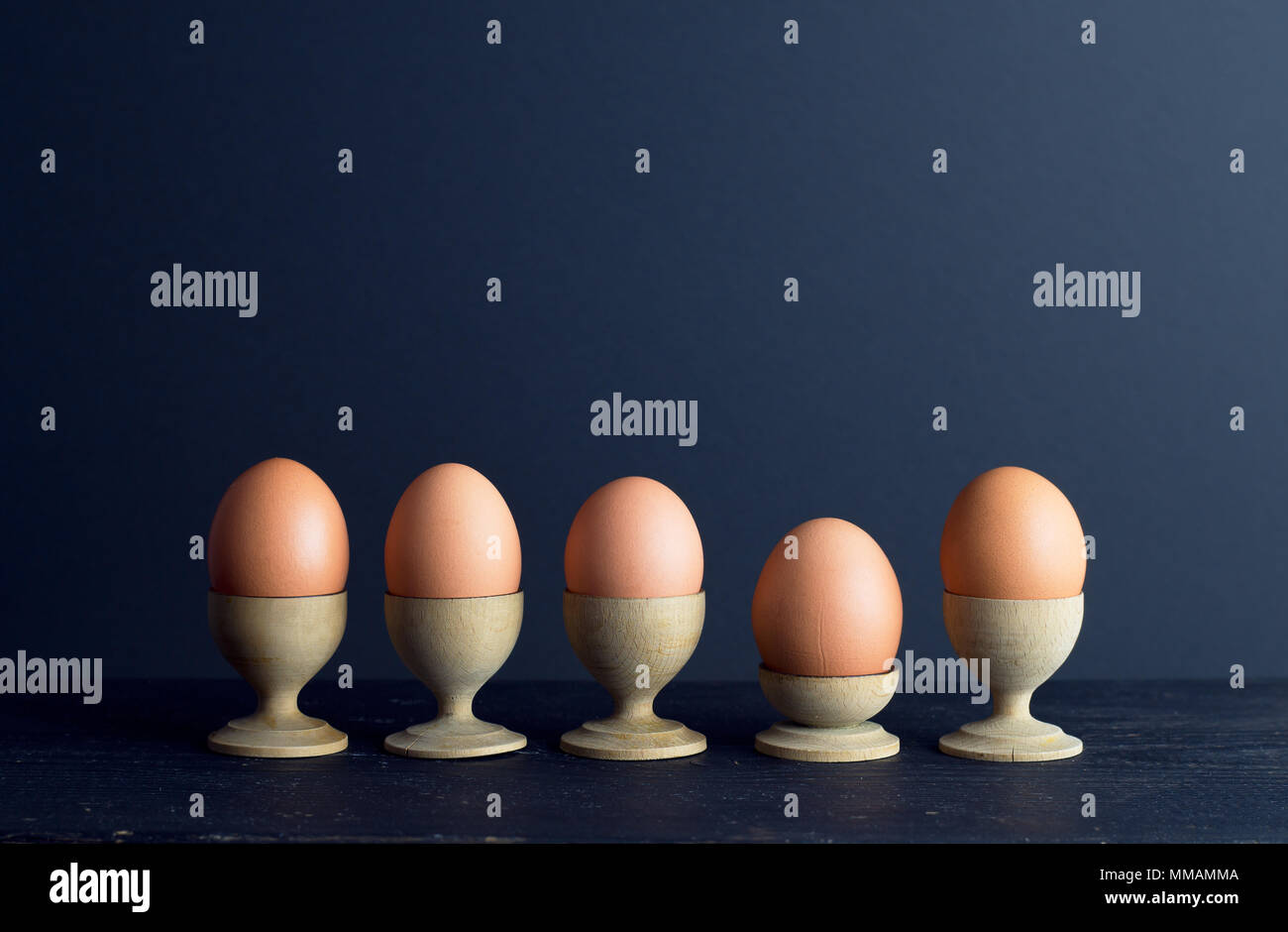Eierbecher mit braune Eier in einer Reihe über dunklen Hintergrund organisiert mit negativen Raum Stockfoto