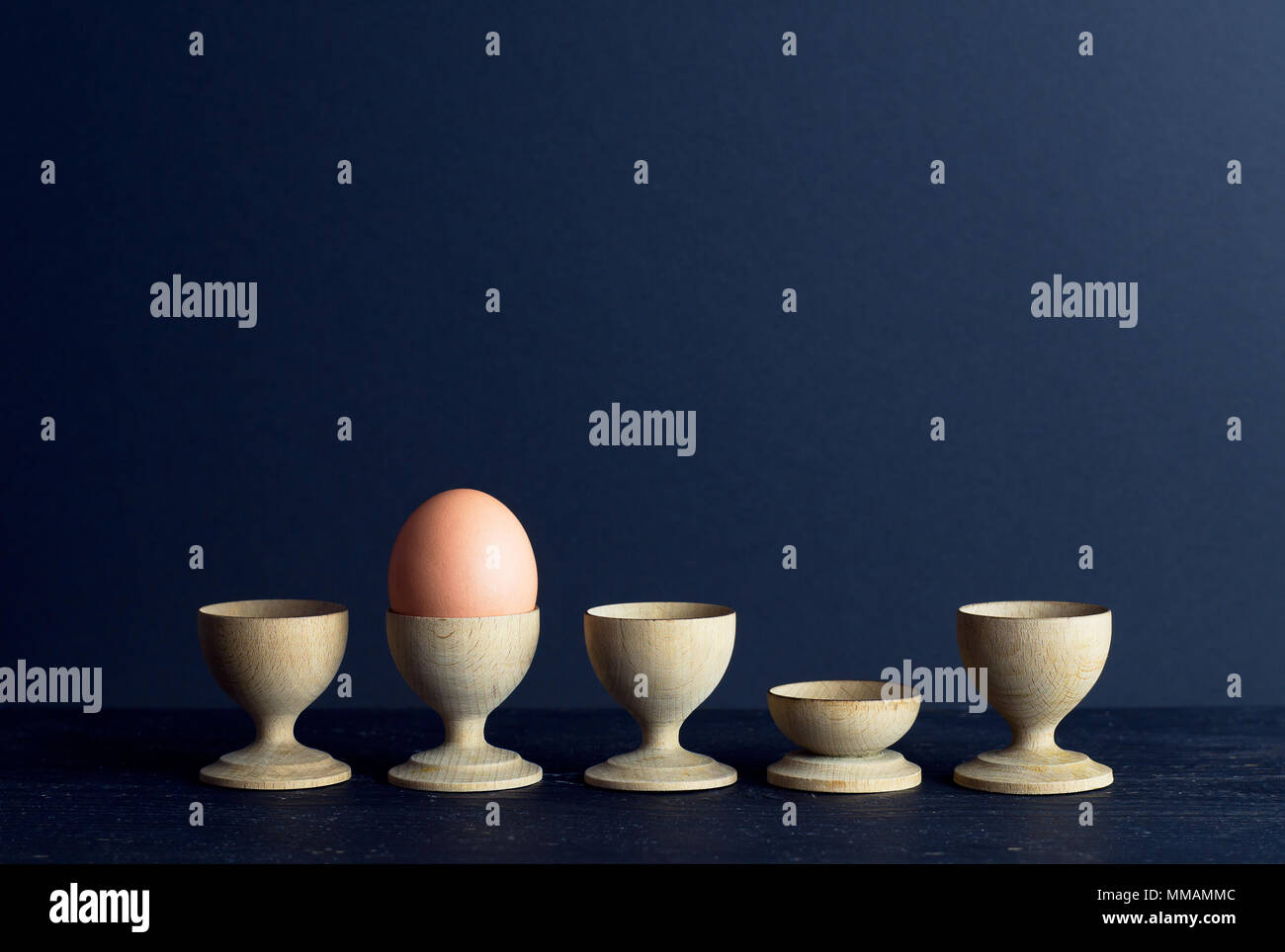 Eierbecher und einem braunen Ei in einer Reihe über dunklen Hintergrund organisiert mit negativen Raum Stockfoto