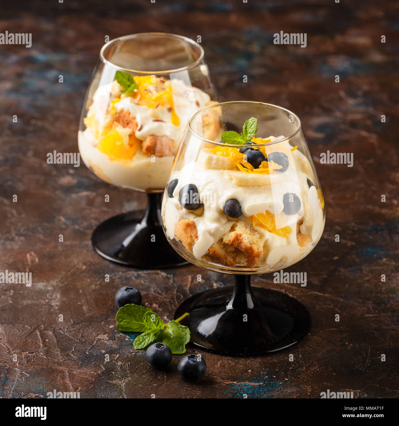 Zwei Gläser mit Gesunden hausgemachte layered Dessert trifle mit Orange, Heidelbeere, Keksen, Joghurt und Müsli Stockfoto