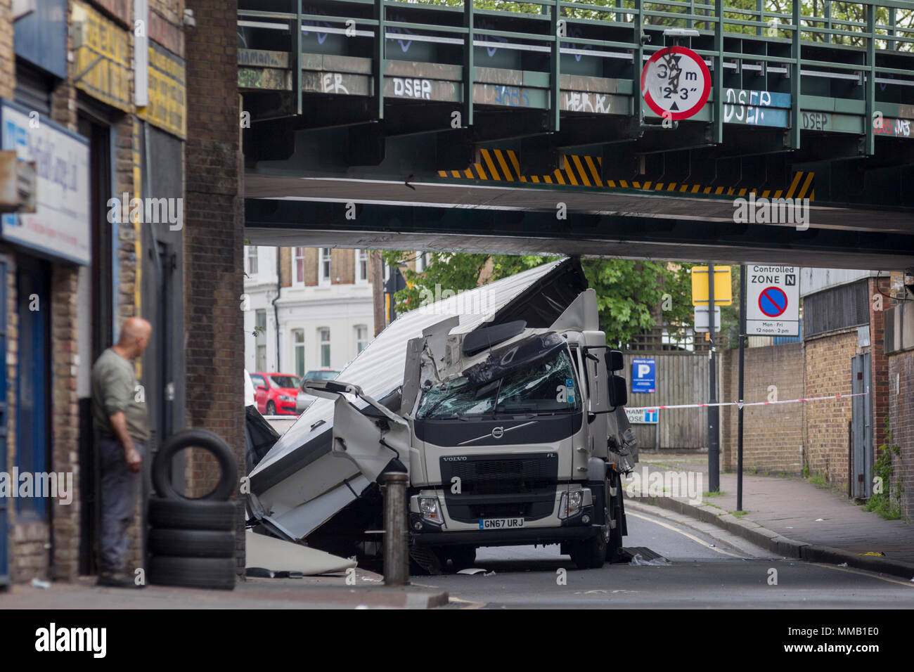 Eine Garage Arbeiter aus einem MoT Testing Center und die beschädigten Nachwirkungen des Lkw an der Universität Loughborough Junction, nachdem es in einem Der eisenbahnbrücken - ein wichtiger Transportweg für Pendler in die Stadt stürzte, am 8. Mai 2018, im Süden von London, England. Wurde eine Person verletzt. Stockfoto