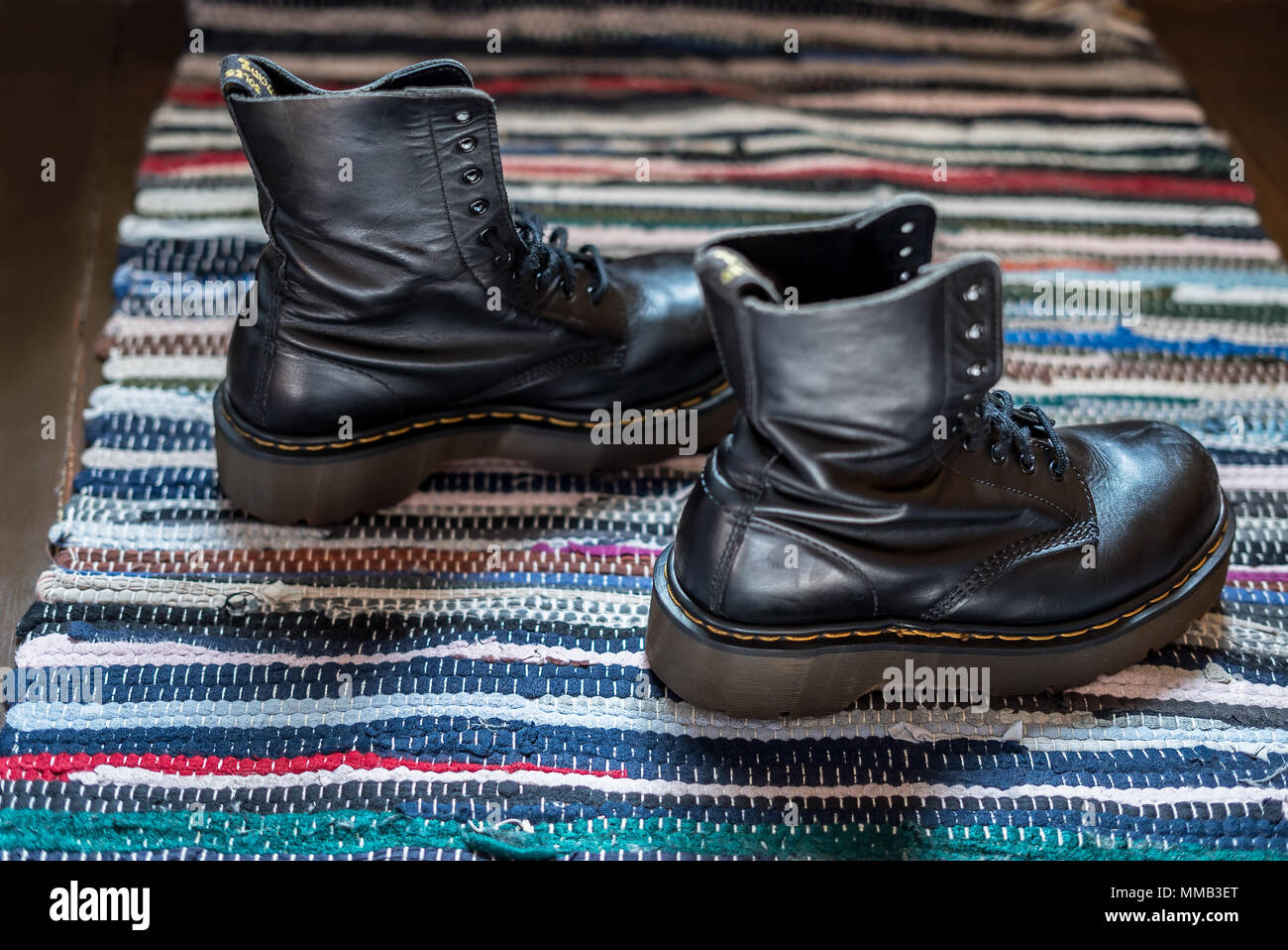 Seitliche Sicht auf zwei robuste, schwarz Knöchel Stiefel aus Leder auf einem bunten Teppich Stockfoto