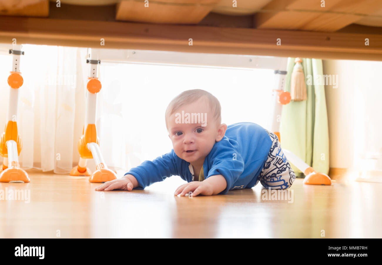 Portrait von niedlichen Toddler boy Kriechen auf dem Boden und Suchen unter dem Bett. Stockfoto