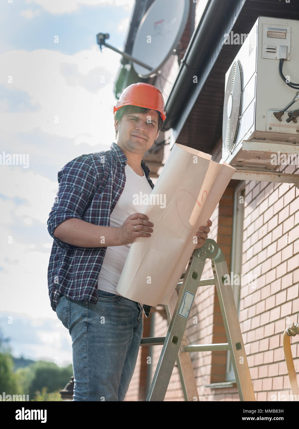 Portrait von jungen männlichen Techniker stehen auf trittleiter mit Blueprints Stockfoto