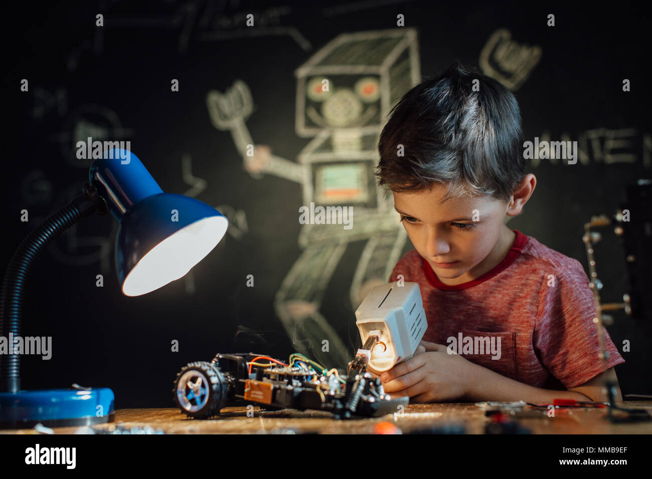 Junge Arbeiten auf seinem elektronischen Projekt mit einem Lötkolben. Porträt eines Schülers sein Hobby genießen und einen Roboter Spielzeug Auto. Stockfoto