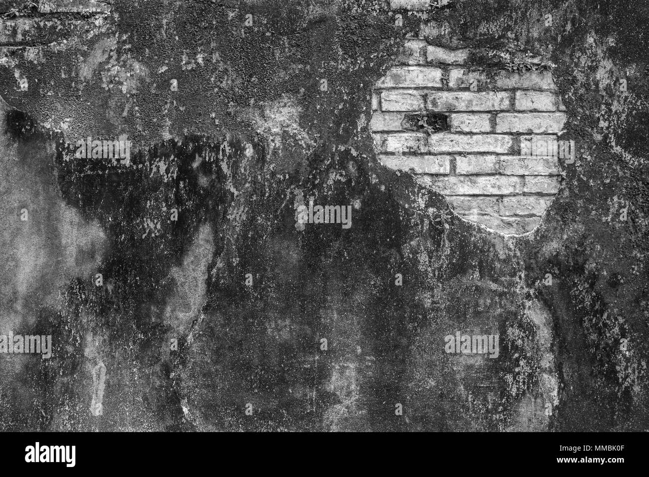 Full Frame Hintergrund einer Verwitterten und beschädigte dunkel grau verputzte Wand in Schwarz und Weiß. Gips ist teilweise abgeblättert enthüllt alten Ziegelsteinen. Stockfoto