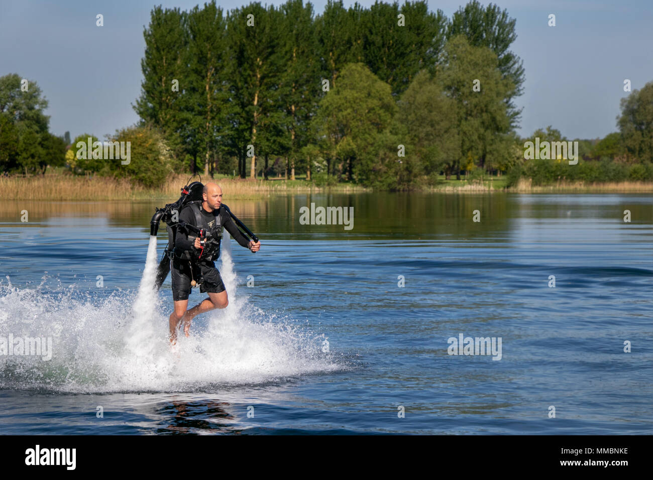 Thrillseeker, athelete zu Jet Lev geschnallt, Levitation schwebt über See mit blauem Himmel und Bäume im Hintergrund. Stockfoto