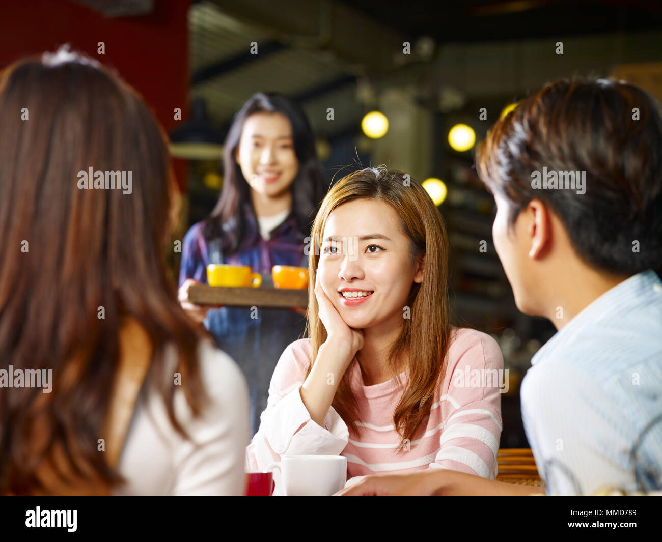Drei glücklichen jungen asiatischen Erwachsene sitzen am Tisch chatten Reden während Kellnerin Kaffee, im Vordergrund Mädchen konzentrieren. Stockfoto