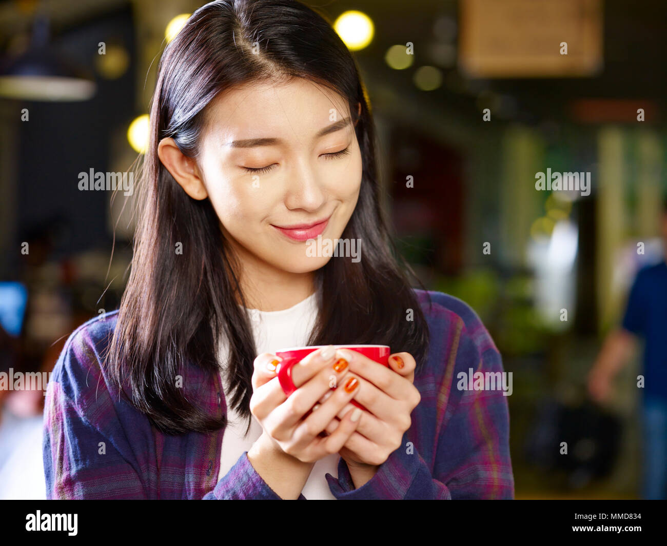 Schöne junge asiatische Frau mit einer Tasse Kaffee lächelnd mit geschlossenen Augen. Stockfoto